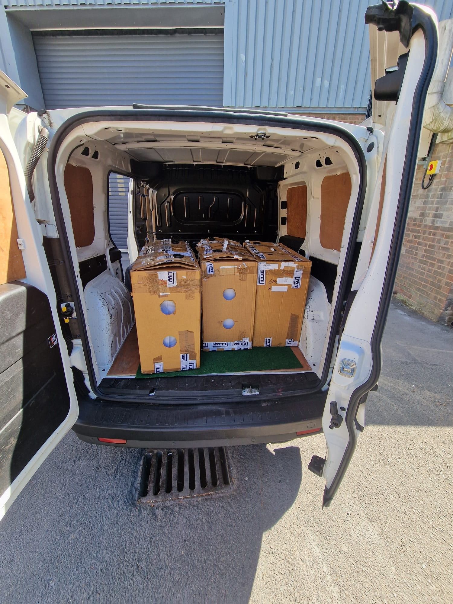 Three large cardboard boxes loaded in the back of a white Fiat Doblo