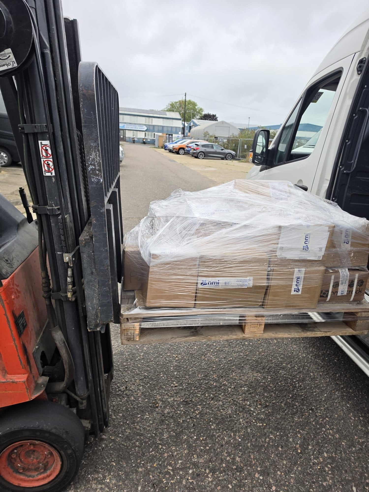 A forklift holding a wrapped pallet next to the open side door of an Encea Transport van